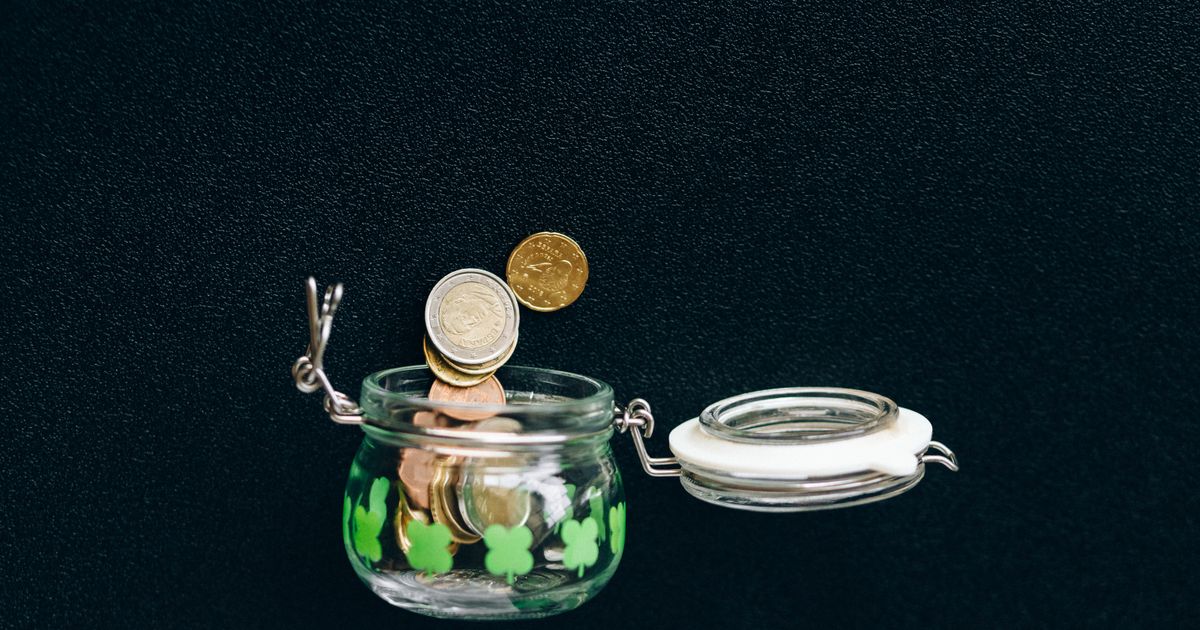 Coins dropping into a glass jar against a black background