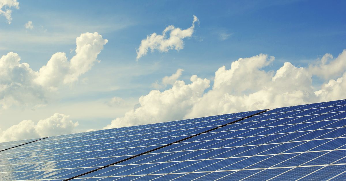Rows of blue solar panels under a bright summer sky with white clouds
