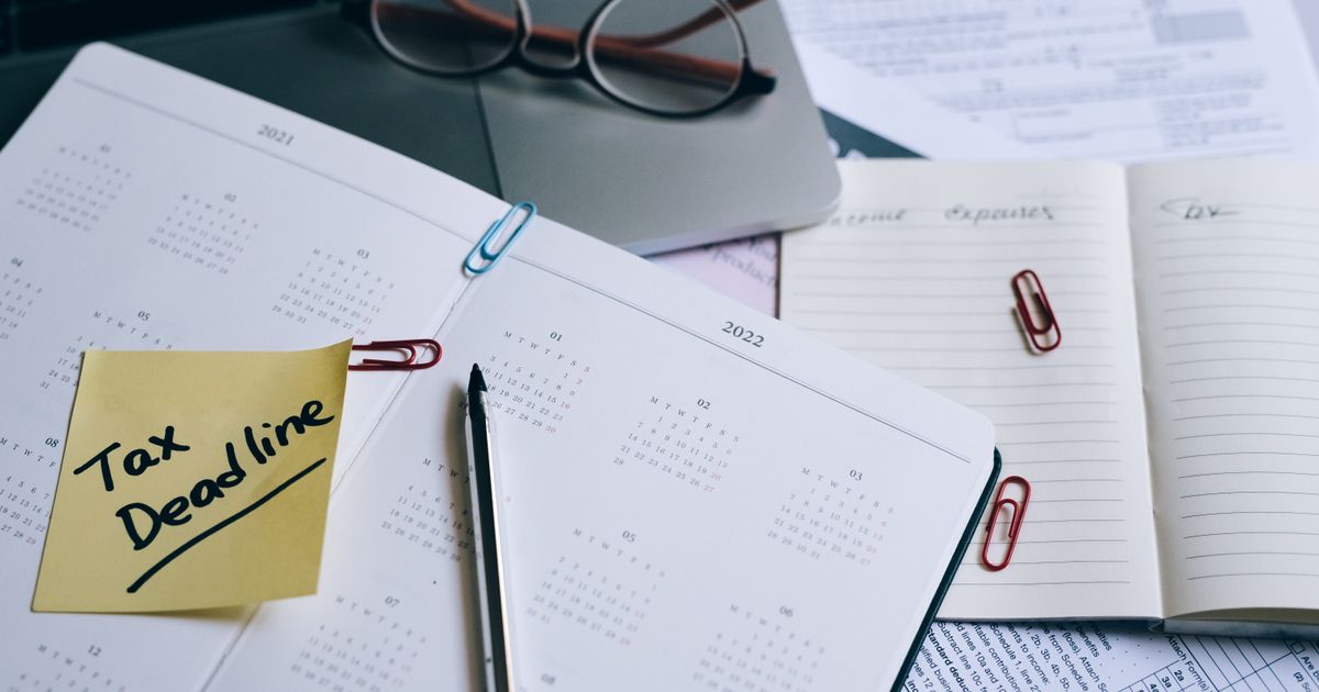 A planner with a yellow sticky note reading Tax Deadline, beside glasses and tax forms